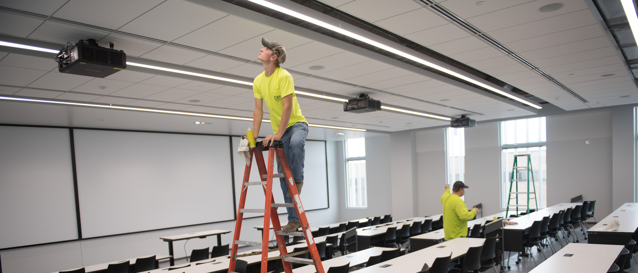 Two employees check the light fixtures in a lecture room in the Seamans Center