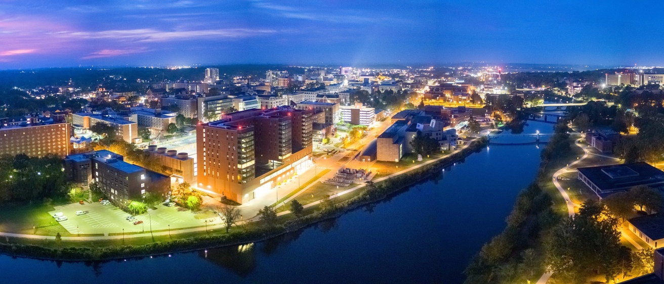 A panoramic photo of the University of Iowa campus taken from above the Iowa River at dusk.